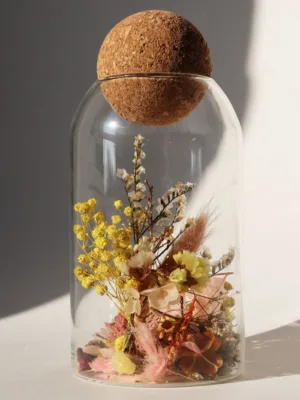 כלי זכוכית מעוצב ומלא בקוקטייל פרחים יבשים טבעיים בצבע צהוב וורוד, פקק שעם כדורי.