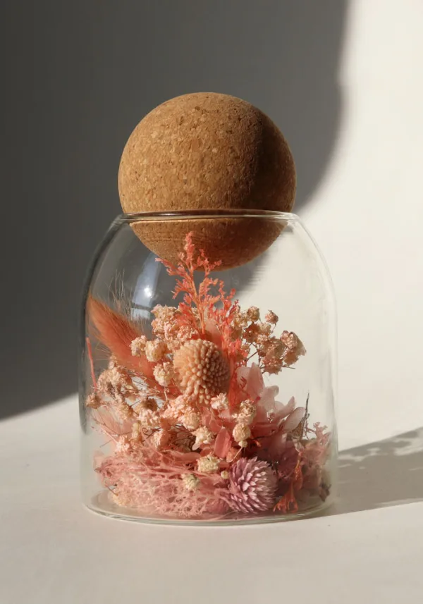 כלי זכוכית מעוצב ומלא בקוקטייל פרחים יבשים טבעיים בצבע ורוד אפרסק, פקק שעם כדורי.